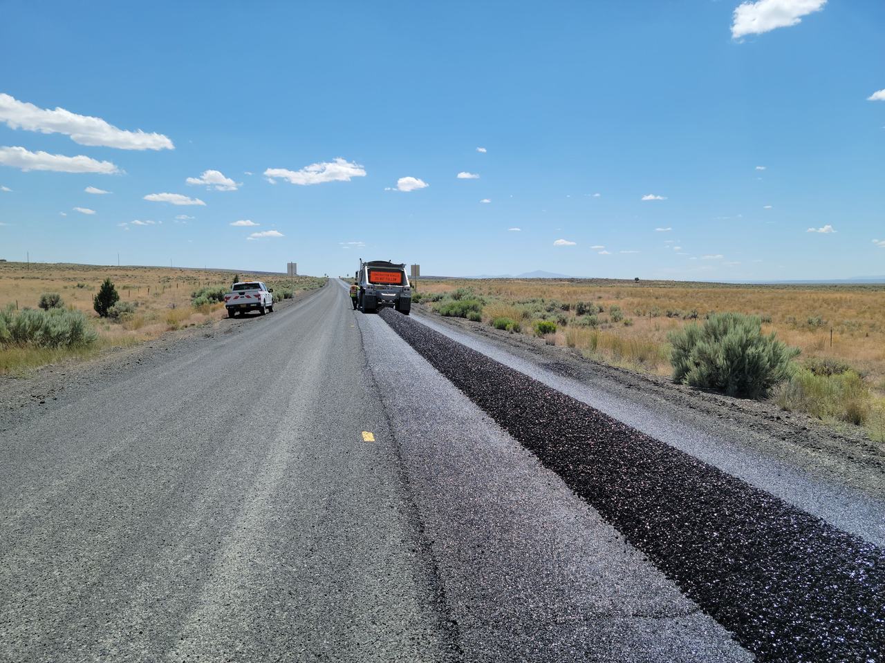 Fresh dark asphalt overlay laid beside the worn grey surface it covers