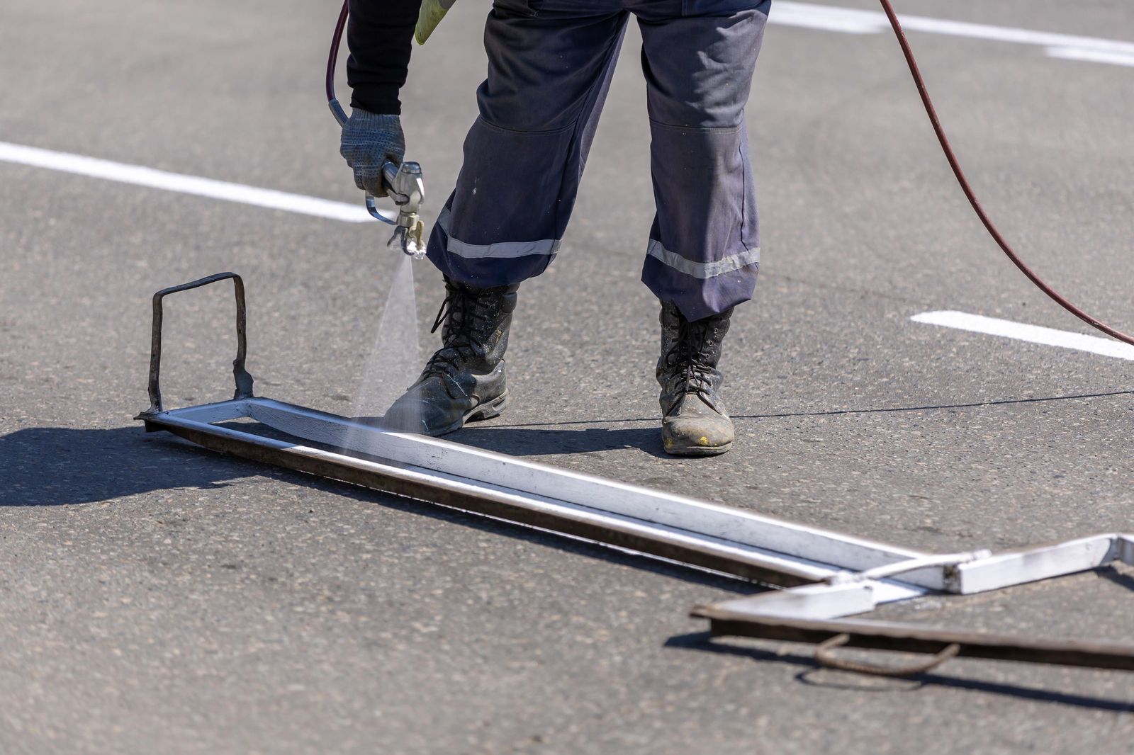 Striping worker spraying a fresh white line along a straightedge guide